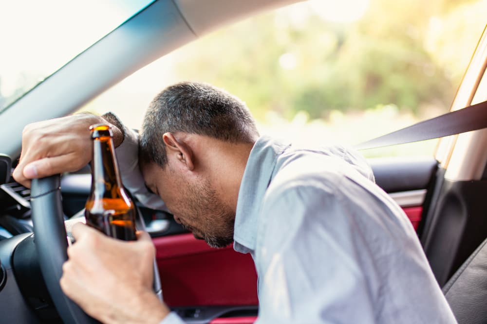 Man resting head on steering wheel while holding a bottle after DUI accident.