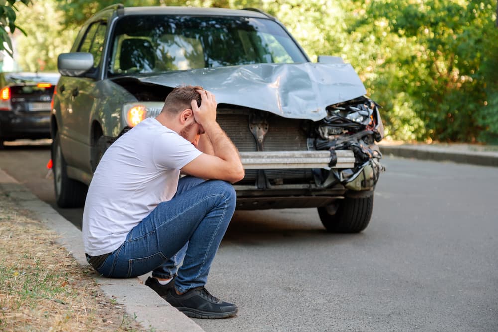 Man sitting next to car after a car accident.