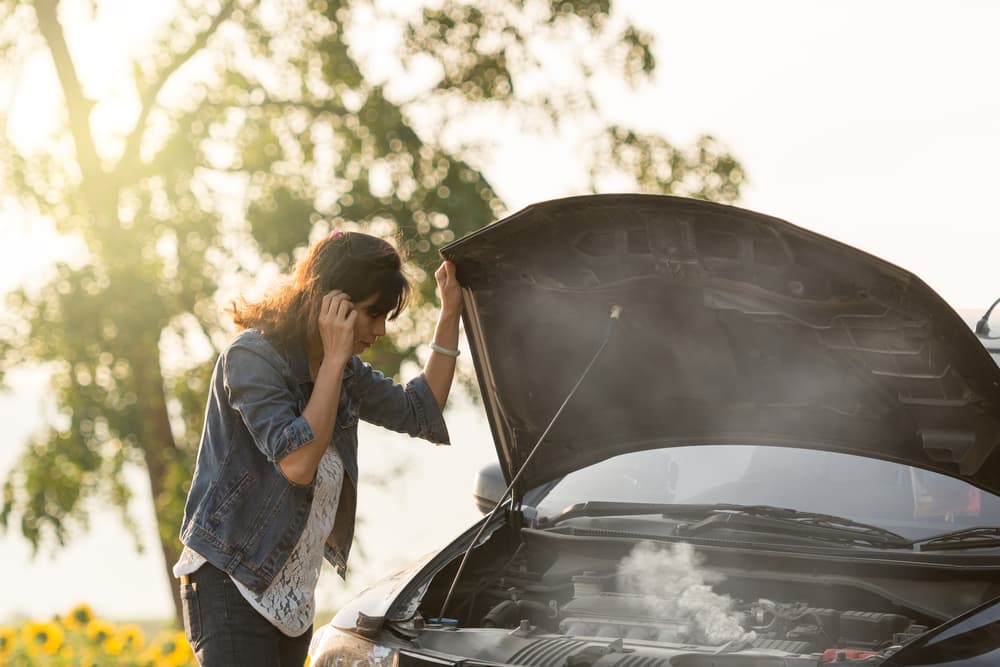 Woman looking into her car that's smoking due to lack of maintenance