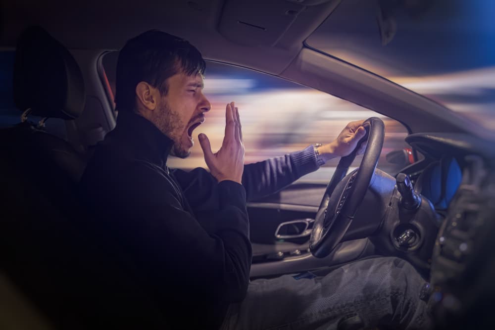 A person yawning behind the wheel of a car showing signs of driver fatigue.