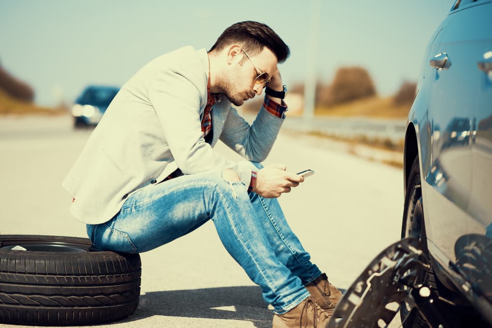 Man sitting on tire after a car accident after a tire malfunction.