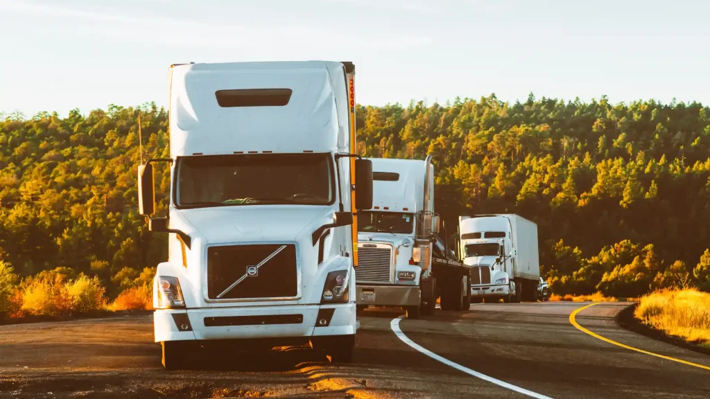 Fleet of semi-trucks driving on a highway with a forest in the background.
