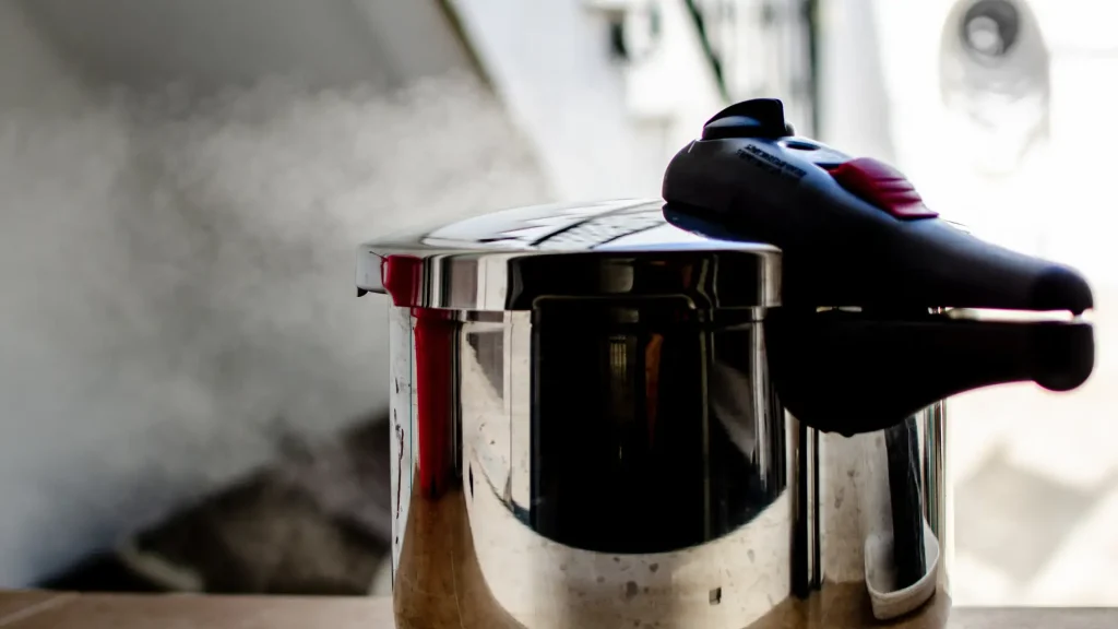 Close-up of a person holding the lid of a pressure cooker with steam rising.