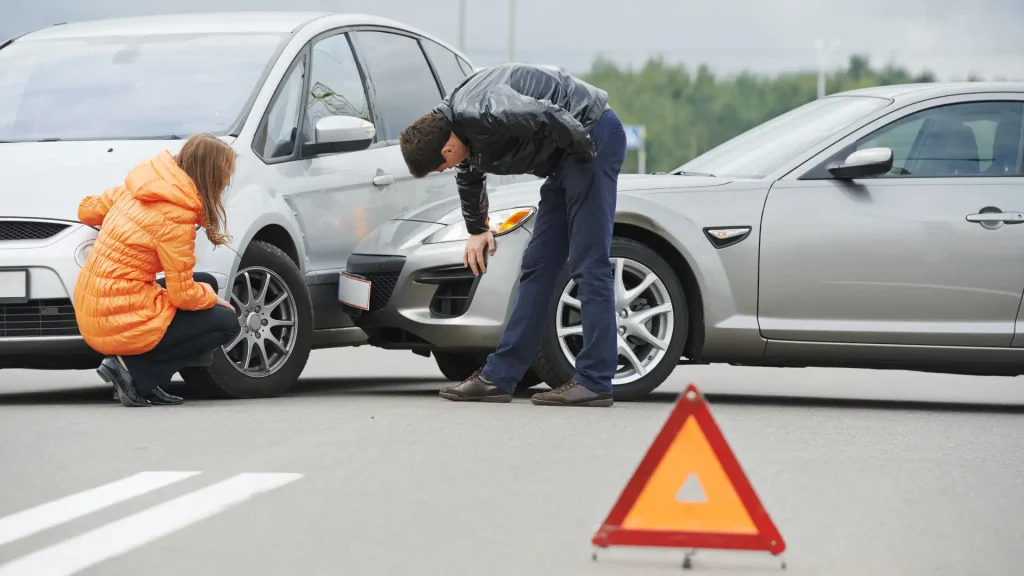 Driver inspecting car damage after a collision with warning triangle placed on road